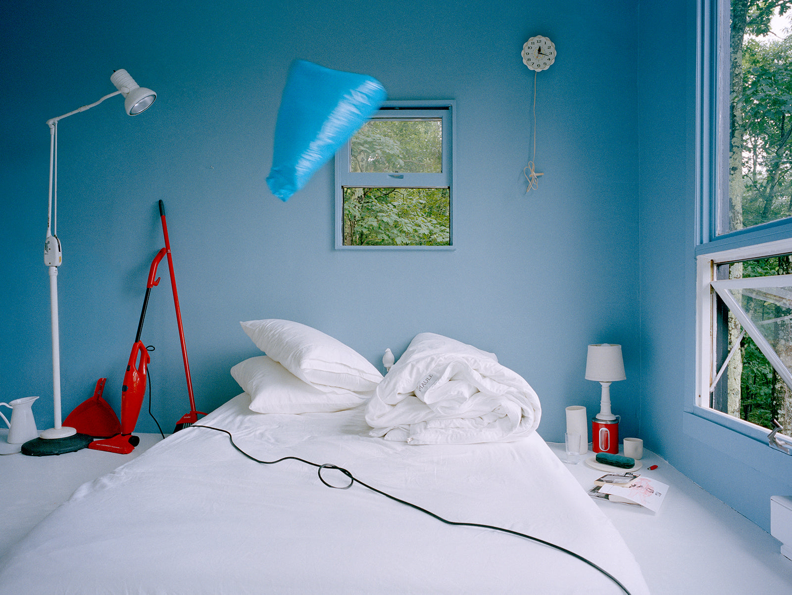  weird bedroom scene with vacuum cord across white bedding and blue bag flying through the air