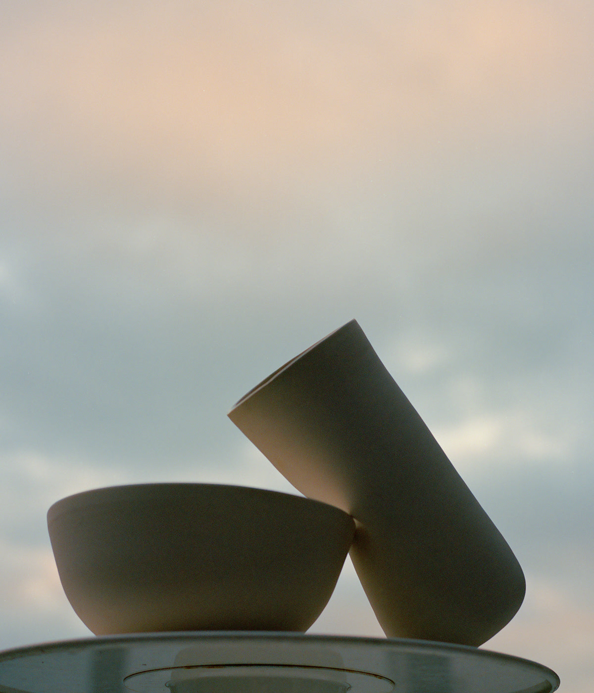  white porcelain hand-thrown ceramics on table against summer evening sky with soft clouds and orange sunset